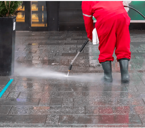 Sidewalk being cleaned by worker in red