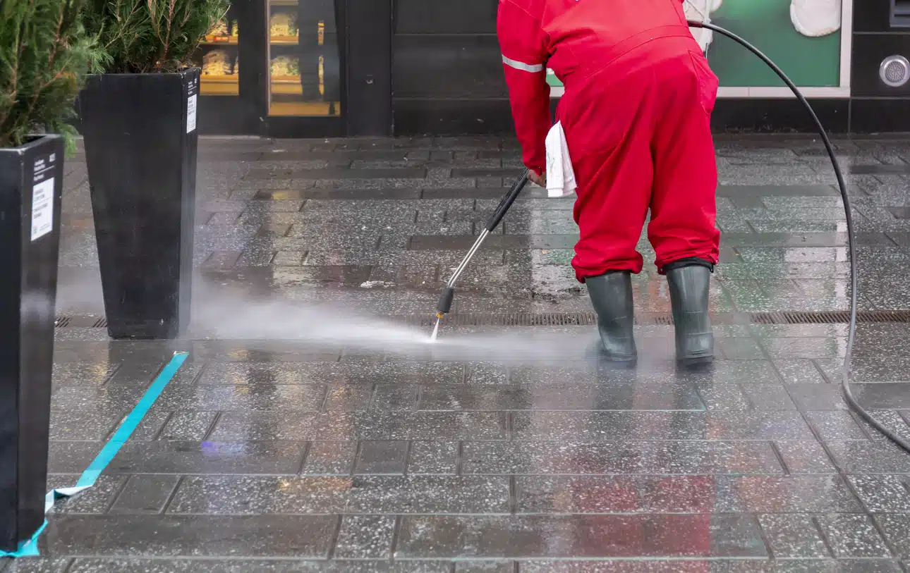 Person cleaning pavement with high-pressure hose