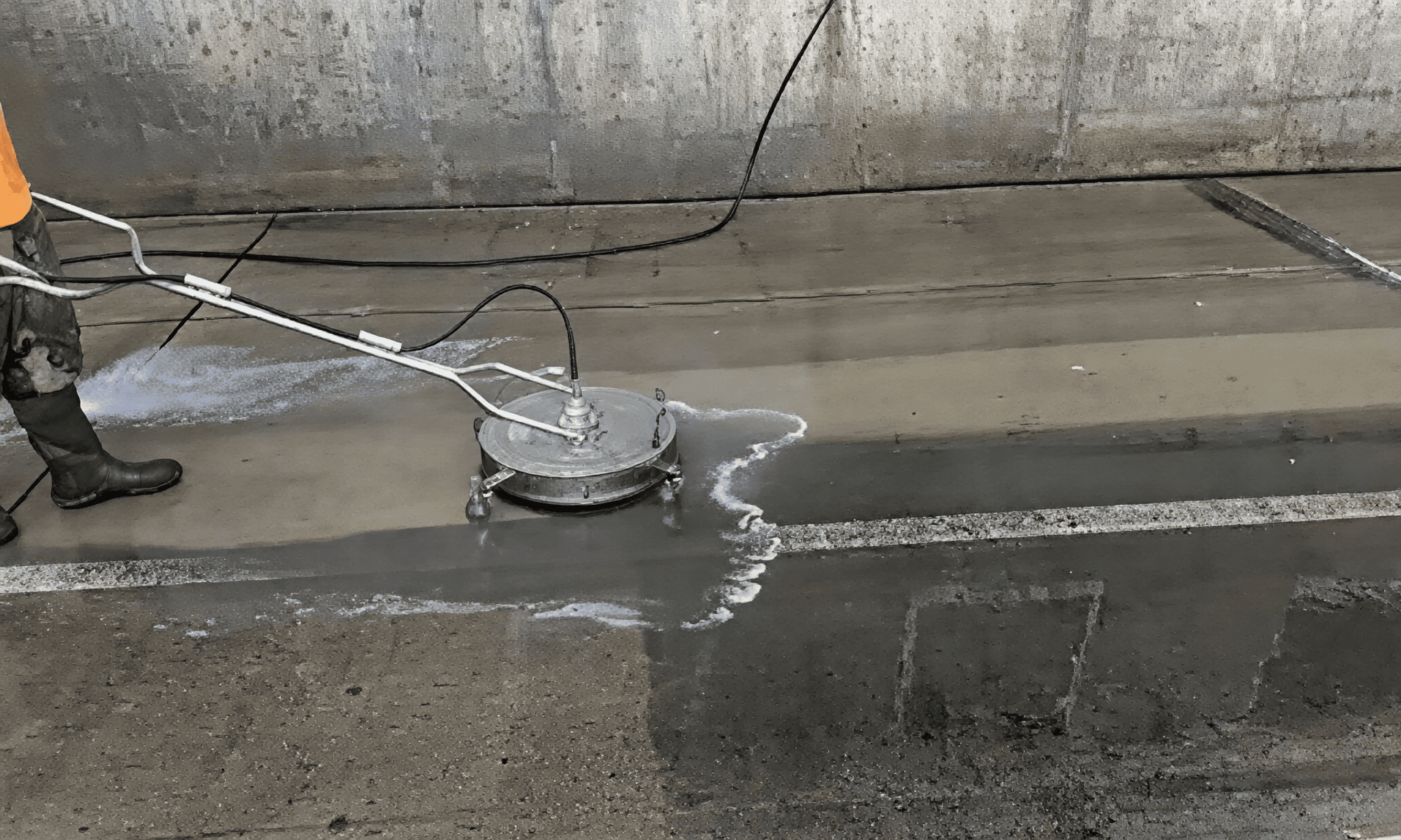 Worker using pressure washer on concrete.