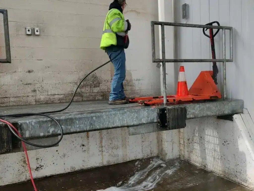 Worker using power washer on loading dock